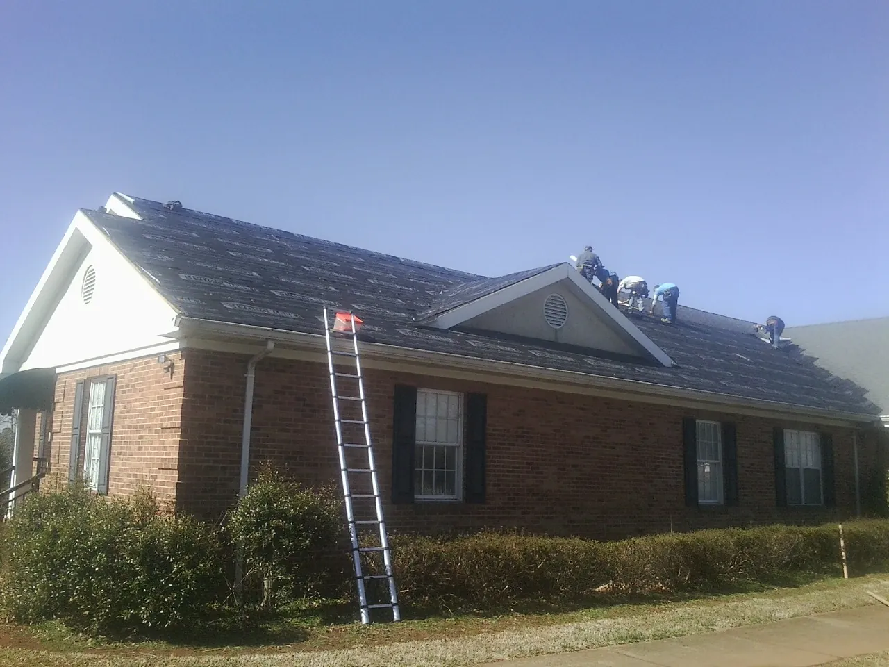 Crew tearing shingles off a brick ranch roof with a ladder set — Emergency Roof Repair work by our crew in Sperry