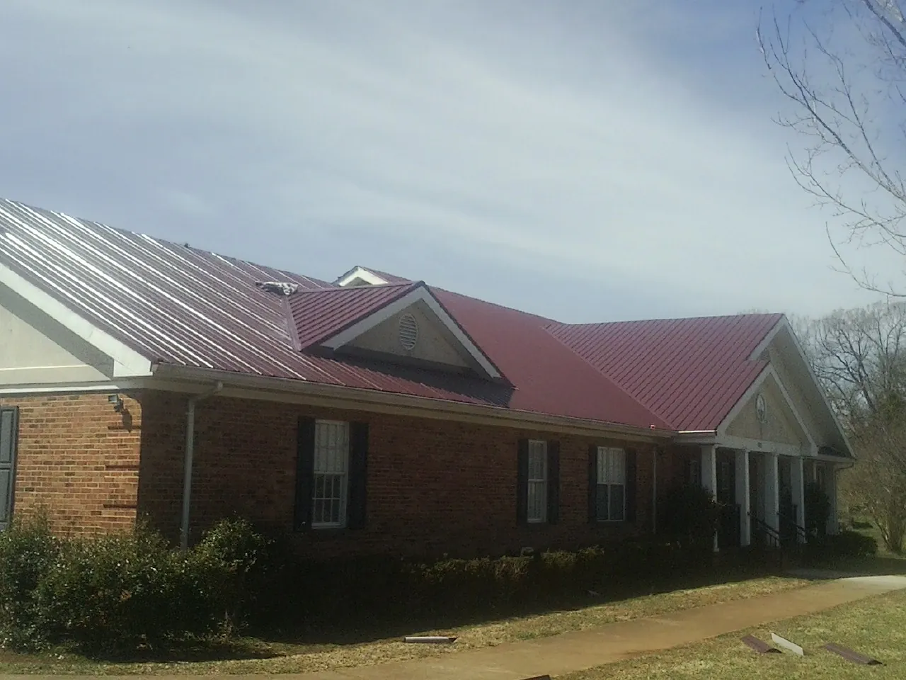 Red metal roof with gabled entries on a long brick building, from a Hail Damage Roof Repair job in Sperry