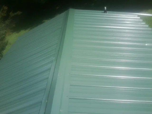 New green metal panels meeting at the ridge of a roof — Flat Roof Repair work by our crew in Sperry