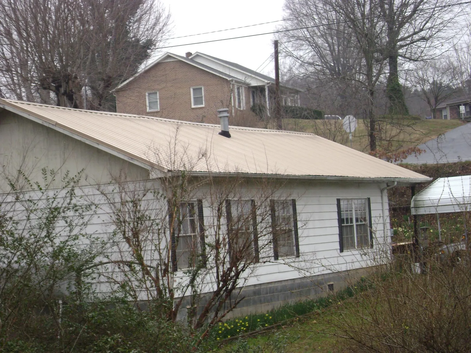 Tan metal roof on a white sided house set into a hillside — Commercial Roofing by Roofing Brothers in Sperry