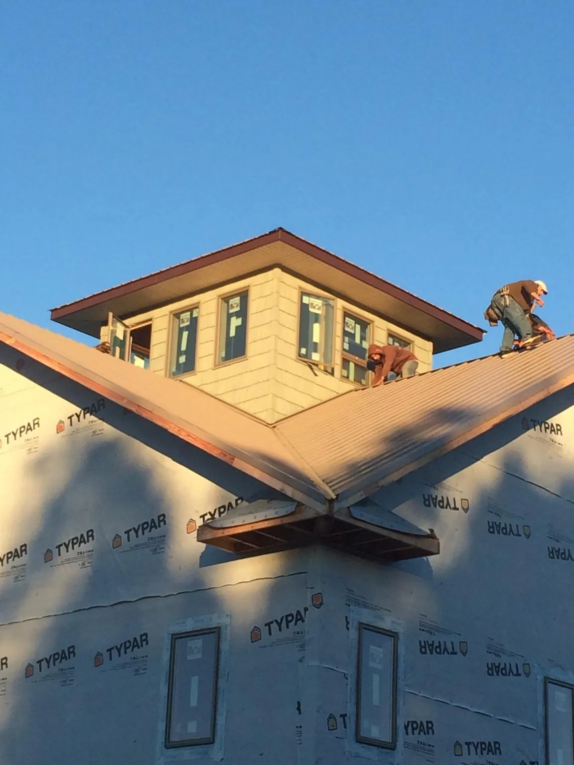 Roofers working around a rooftop cupola on a new metal roof at sunset — Roof Waterproofing in Sperry by Roofing Brothers